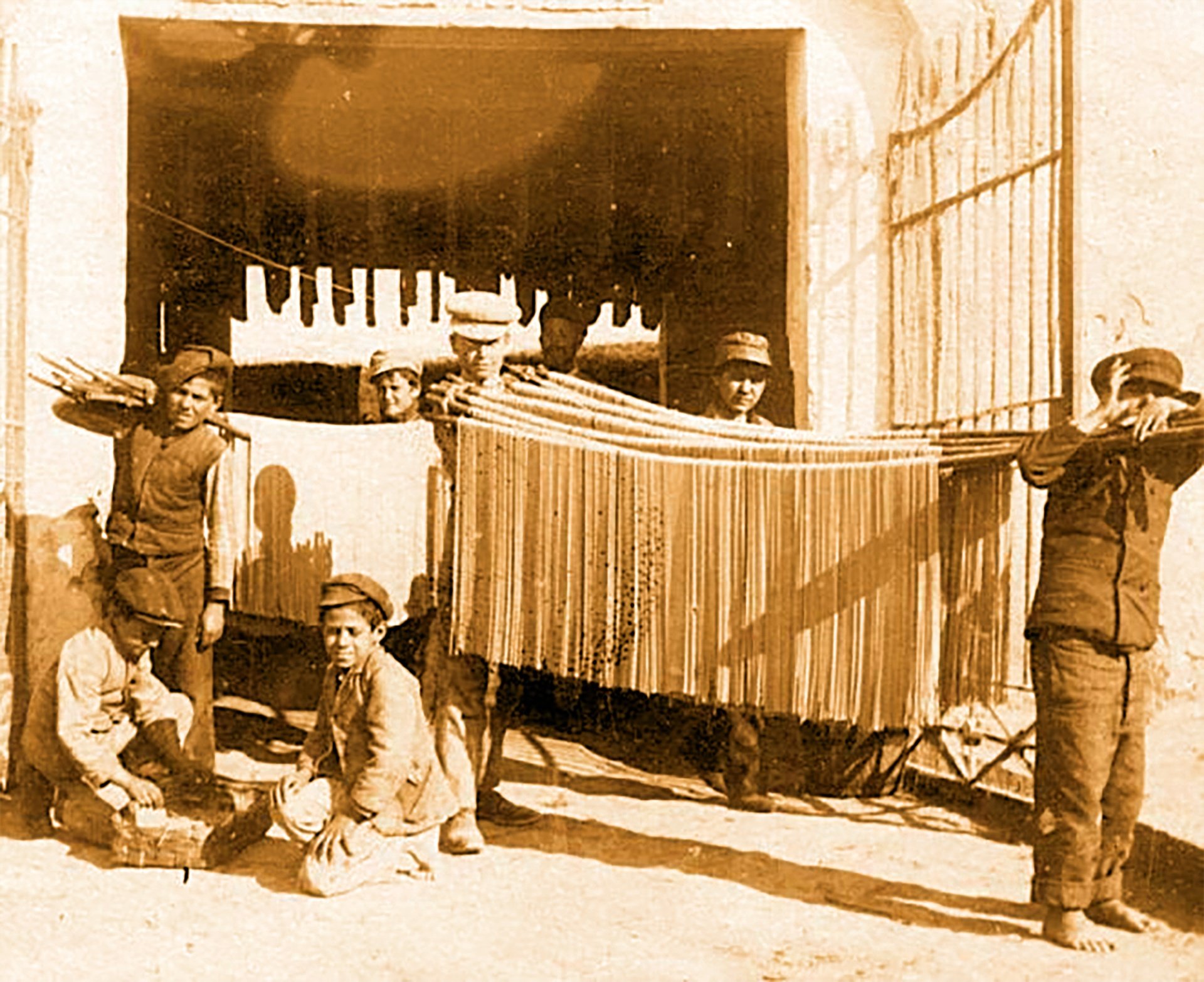 Sepia photograph of pasta-makers drying spaghetti in Gragnano in the early 20th century